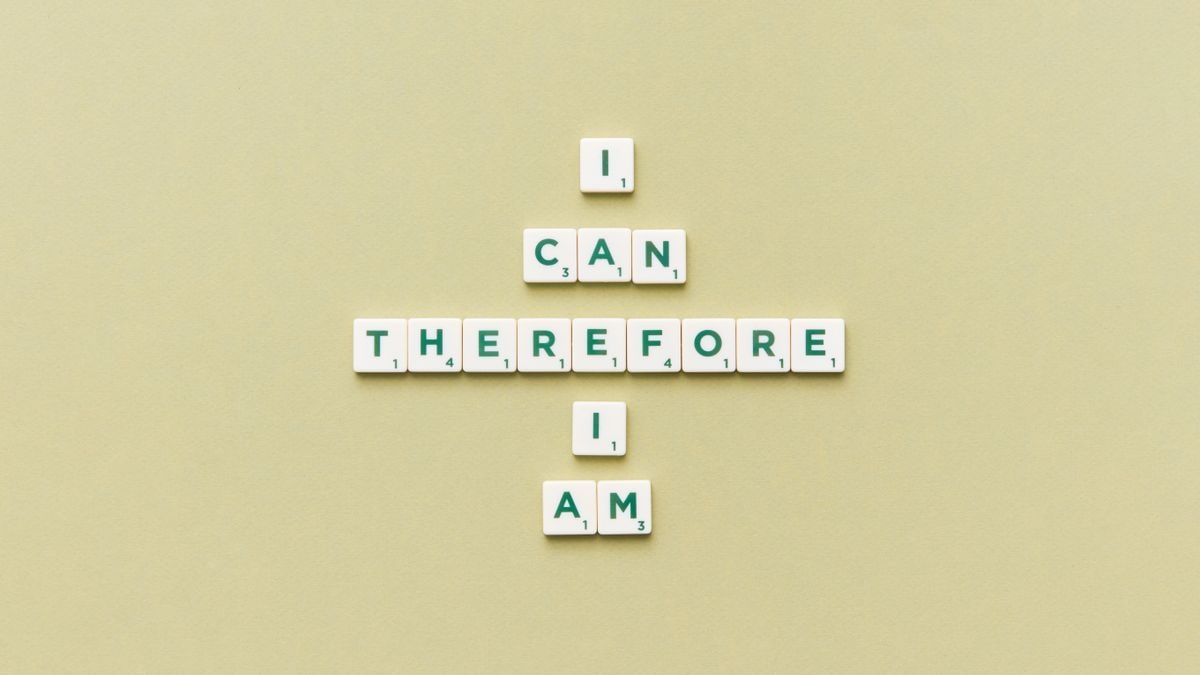 Inspirational phrase 'I Can Therefore I Am' arranged using Scrabble tiles on a green background.